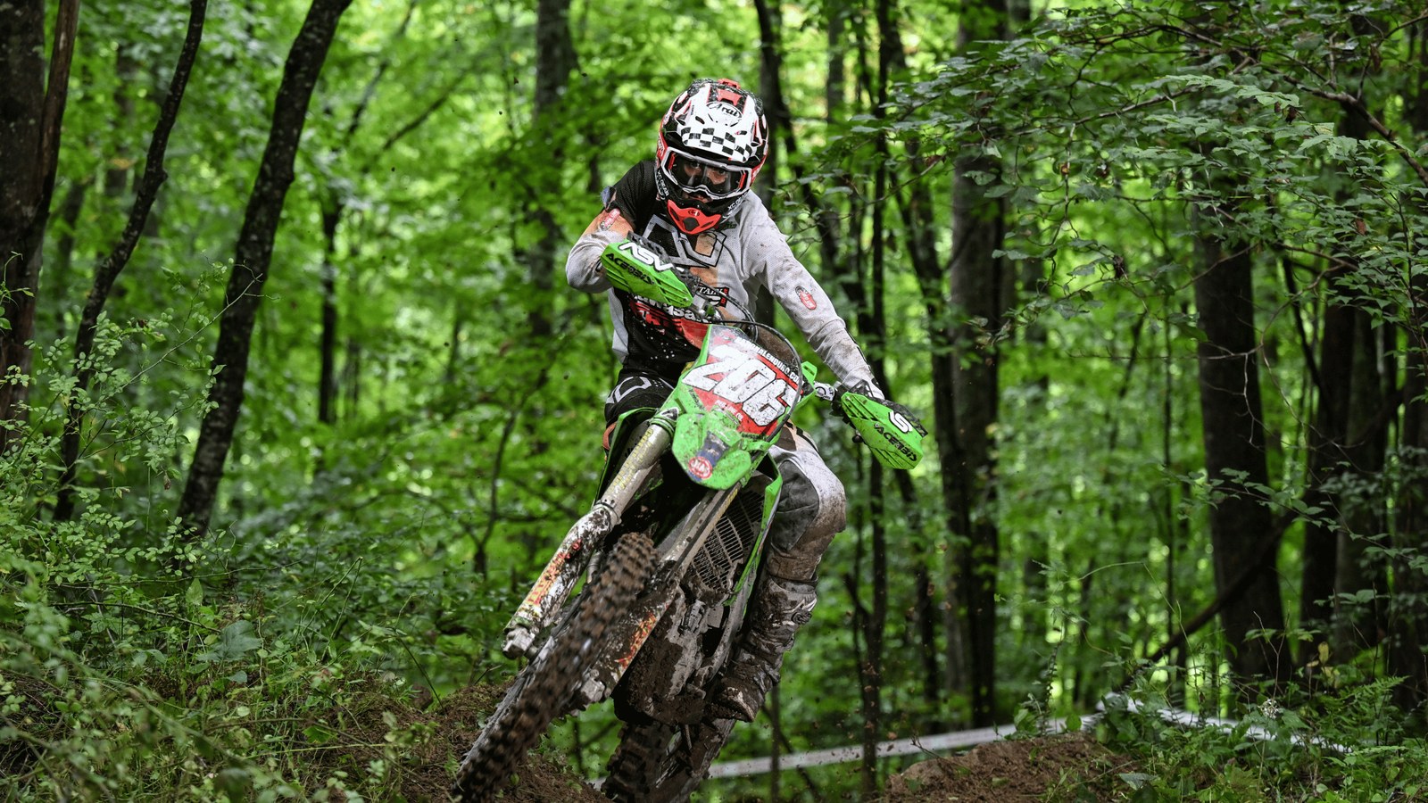 Rocky Mountain ATV/MC Red Bear Kawasaki rider in a checkered helmet climbing through the West Virginia woods at the 2026 Burning Rock National Enduro