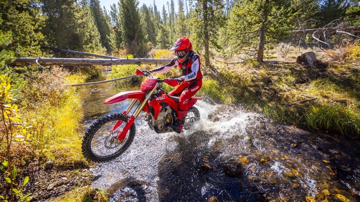 Ducati Desmo450 EDX rider splashing through a forest creek crossing, from the launch ride rather than the race