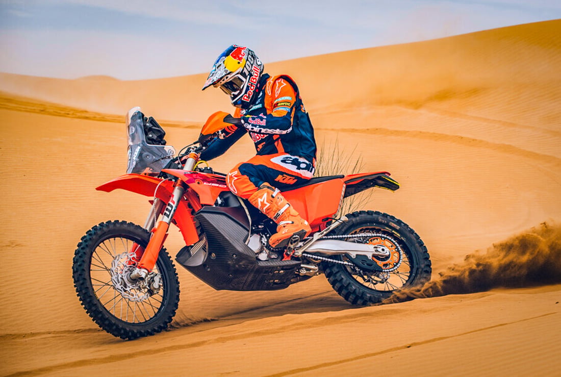 2027 KTM 450 Rally Replica roosting sand dunes — nav tower and multi-tank rally bike readable