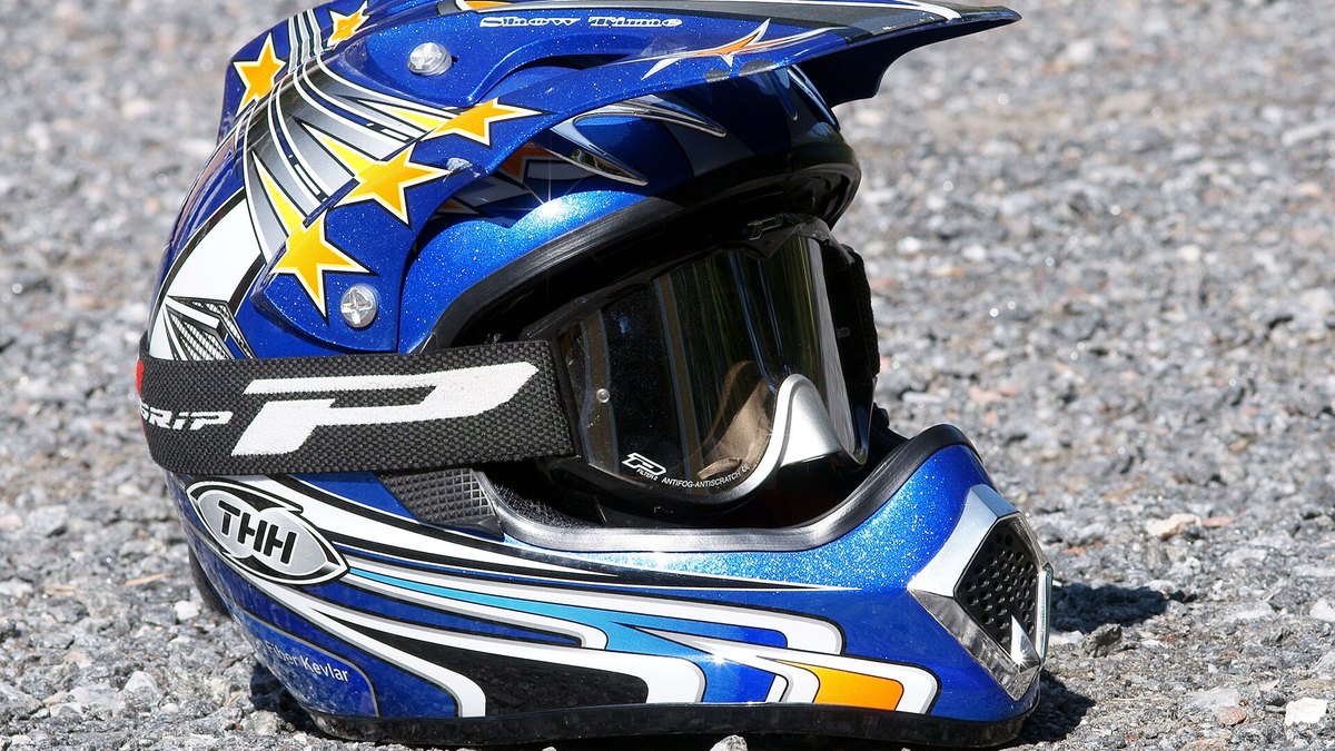 Off-road helmet with peak and goggles resting on gravel