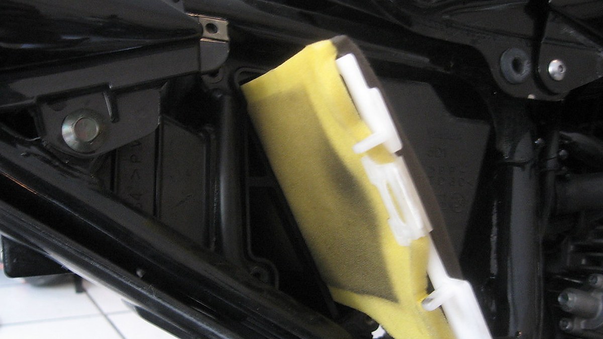Yellow foam motorcycle air filter on white plastic cage, partially pulled from airbox - dirt-bike foam filter cleaning