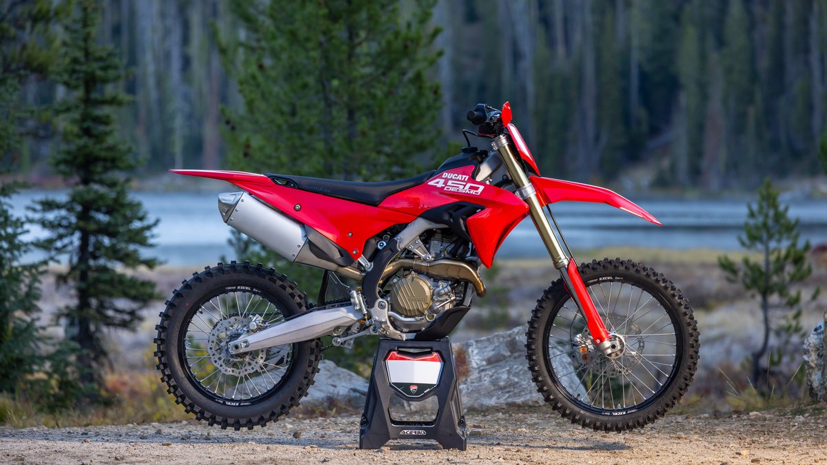 Red Ducati Desmo450 EDX on a stand beside a lake and pine trees