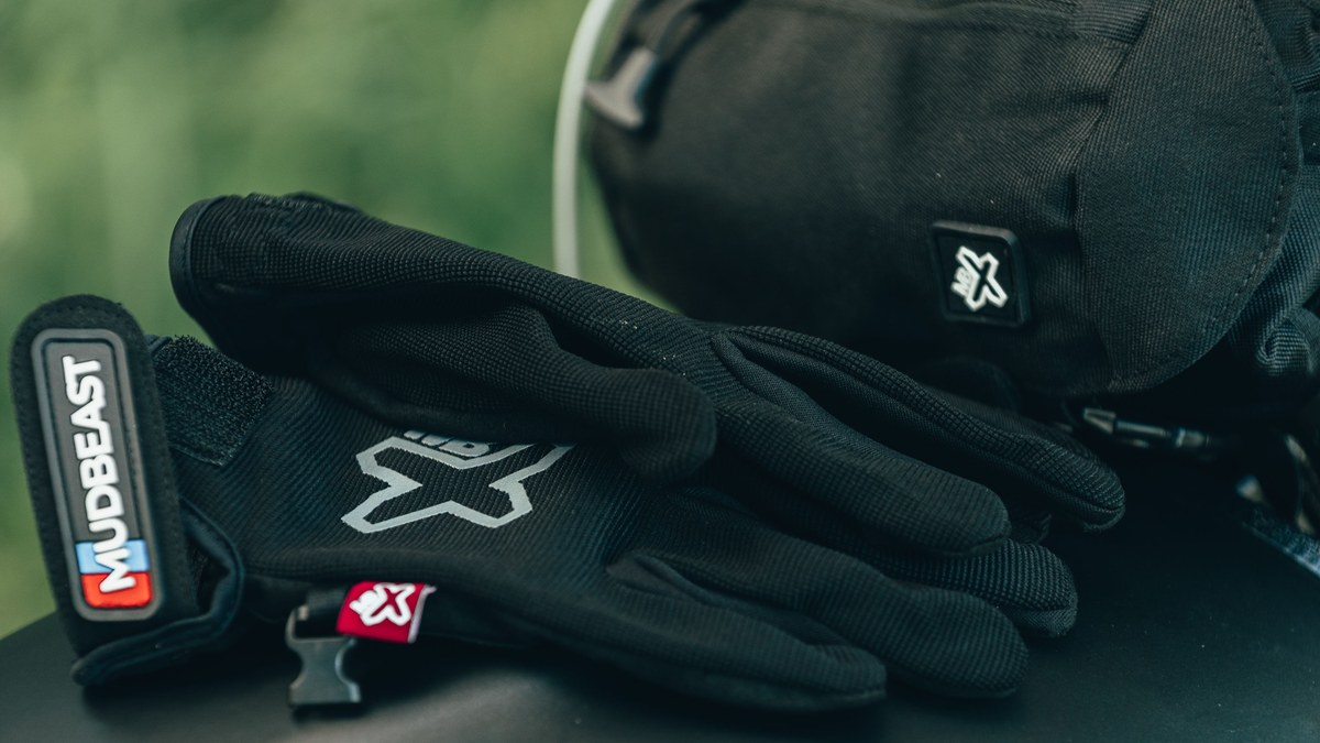 Pair of black lightweight dual-sport / trail motorcycle gloves with wrist strap resting outdoors