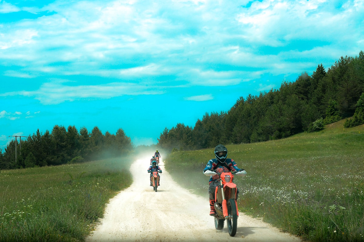 Enduro dirt bikes riding a dusty trail past forest edge — interim Sunday Creek woods character